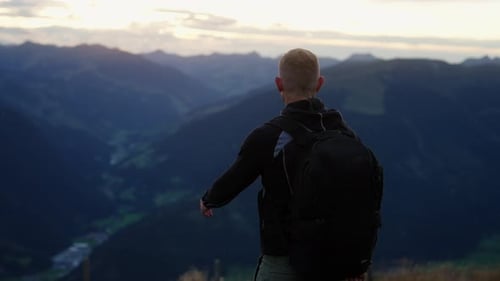 Back View Of Man Pointing Towards Mountains At Sunset