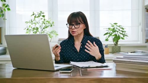 Middle Aged Woman at Work in Home Office Talking on Video Using Computer