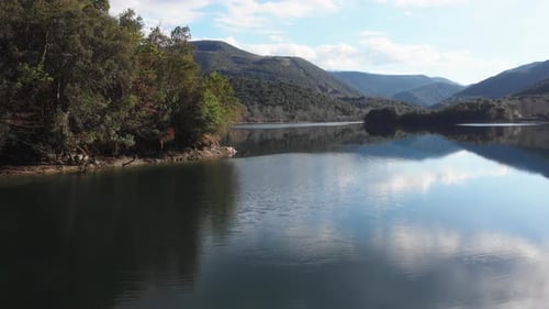 Low altitude drone flying forward over Mountain lake sunny summer day peaks distance