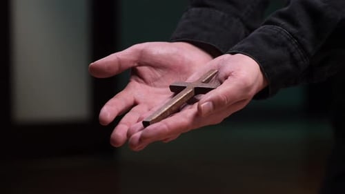 Hands Holding Simple Wooden Cross in Dark Setting