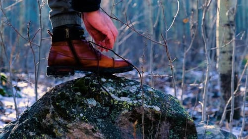 Man Tying Hiking Boot Laces on Forest Rock