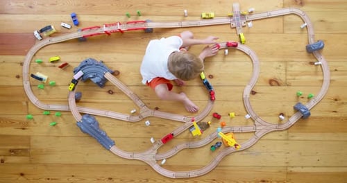 Child Playing with Toy Trains on Wooden Floor
