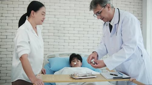 A white doctor advises medicine to Asian mum of a patient boy in the hospital.