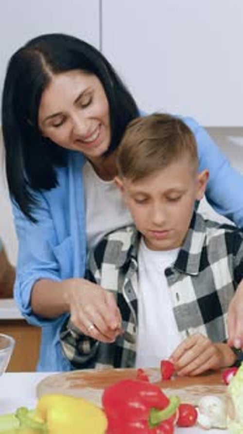 Smiling Woman Teaching Boy to Cut Vegetables in Kitchen