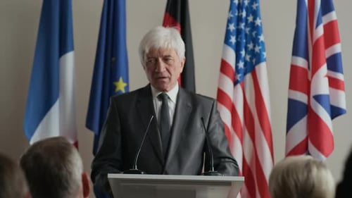 Man Speaks at Podium with Flags in the Background
