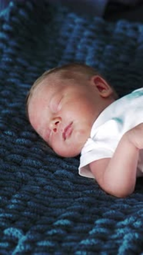 Beautiful newborn Caucasian baby in white bodysuit. Tiny child sleeping on the blue blanket.
