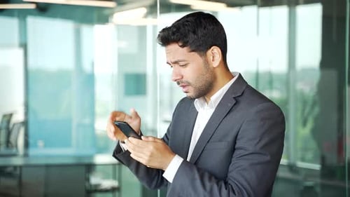 Side view. Frustrated stressed young businessman in a formal suit reads bad news on smartphone