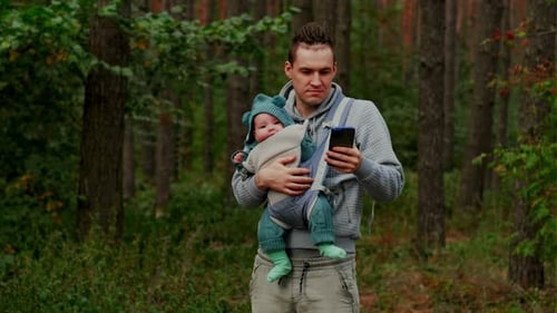 Father and Newborn Baby in a Sling in the Autumn Forest Man with Mobile Phone Happy Family