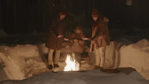Parents and Son Standing around Fire Outdoors on Winter Night