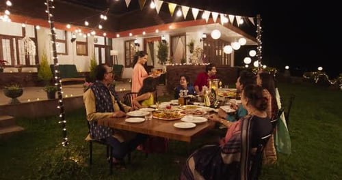 Happy Extended Indian Family Eating Dinner Together in a Fancy House Garden at Night. The