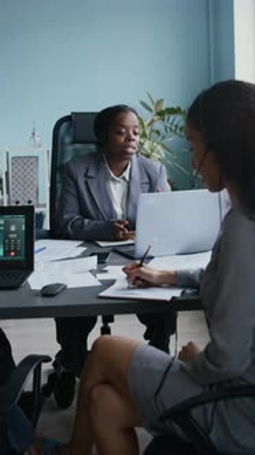 Operator Consulting Online Consumers in front of Colleague Taking Notes