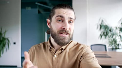 POV Smiling businessman talking on a video call using a phone in modern business office. Handsome
