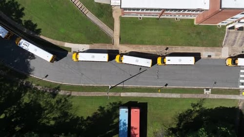 Row of yellow school buses in front of school campus. Arriving at historic school in at midday.