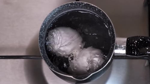 Zwei Eier werden in kochendem Wasser auf einem gasgrauen Herd in der Küche gekocht, Nahaufnahme von oben, Morgen