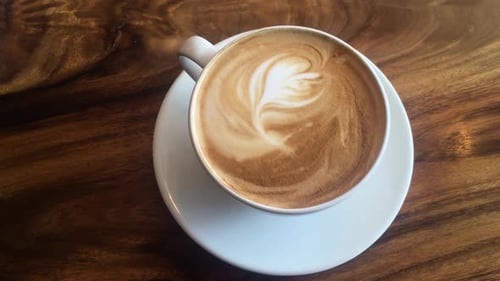 Latte art in white cup on wooden background, closeup, slow zoom, high angle