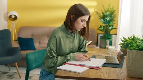 Woman Studies Documents at Table with Laptop