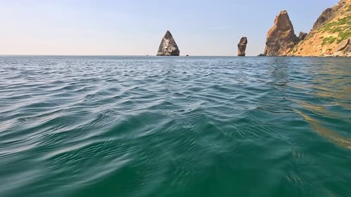 Sea Water Surface Camera Flies Over the Calm Azure Sea with Volcanic Rocky Shores on Background