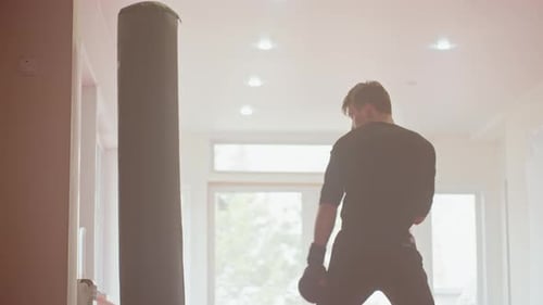 Athlete Wearing Gloves Practices Boxing Strikes on Punching Bag Inside Bright Gym