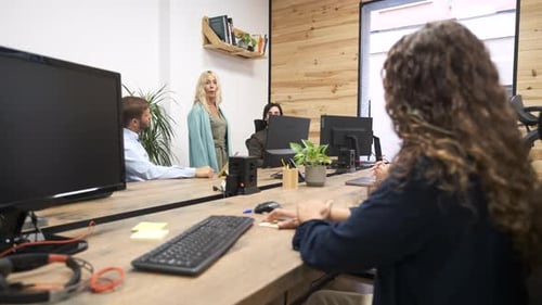 Gerente feminina madura conversando com a equipe sentada em mesas de computador em um escritório criativo