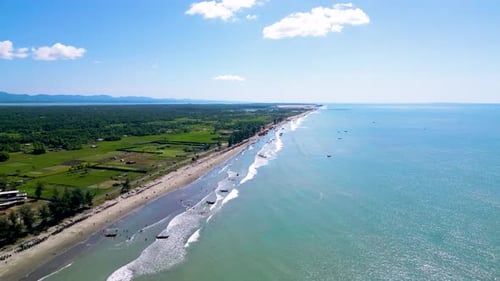 Luftaufnahme des langen Küstenstrandes mit Fischerbooten und viel Grün