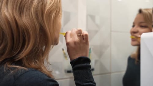 Young Woman Brushing Teeth in Bathroom Mirror