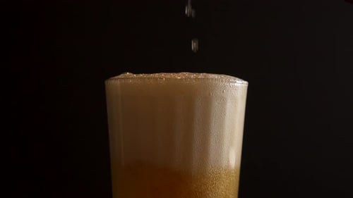 Pouring beer into a glass half full of foam, close up slow motion