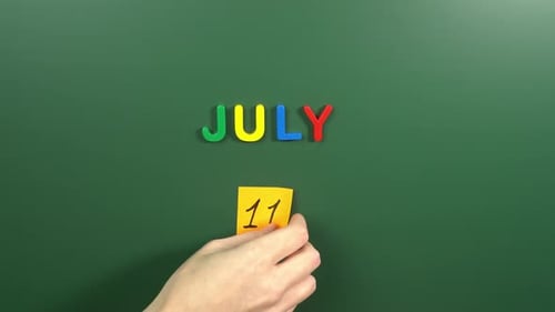Hand sticking a sticker 11 July calendar day on school board. 11 date of July. Eleventh day July