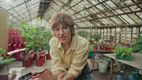 Woman Talking in Greenhouse Surrounded by Potted Plants