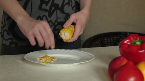 Person Removing Corn Kernels from Corn Cob