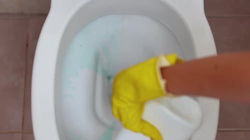 Cleaning Toilet Bowl with Cleaner and Yellow Gloves