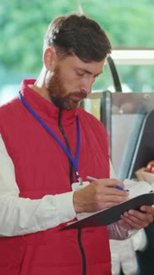 Man Writes on Clipboard Indoors Wearing Red Vest