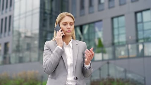 Businesswoman talking on the phone while standing on the street near an office building. Сonfident