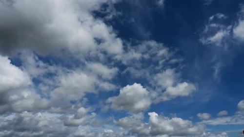 Timelapse of clouds white and grey appearing and disappearing against a blue sky.