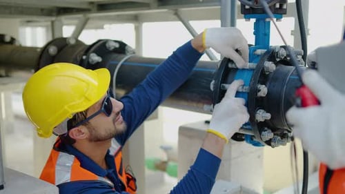 Männliche und weibliche Wirtschaftsingenieure inspizieren in einer Fabrik ein großes blaues Rohrventil. Teamarbeit