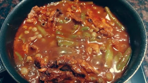 A pot filled with simmering hearty stew containing green beans and meat in tomato sauce, home cookin