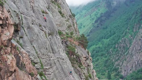 Mountaineer Slowly Scales a Steep Cliff Face with a Partner Belaying From Below