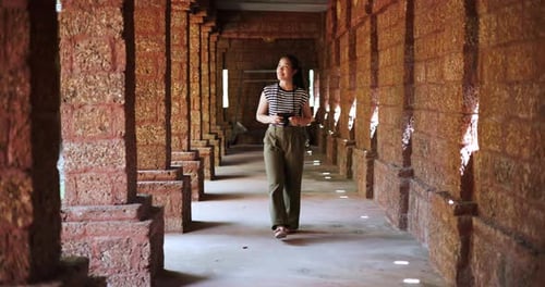 Young Asian woman walks around an ancient site and takes photos with her camera.