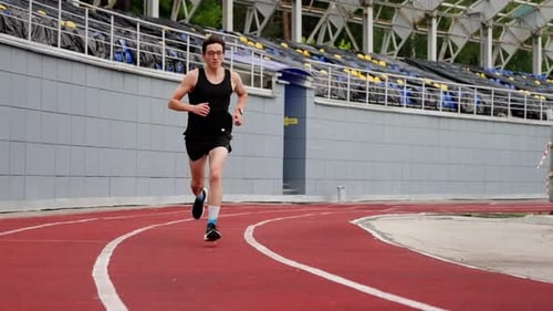 a Guy in a Black Tshirt Black Shorts Black Sneakers Runs Through the Stadium with a Red Coating Slow