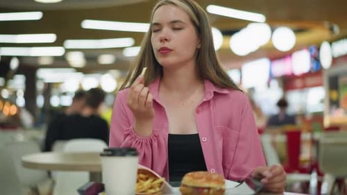 Woman Enjoys Fries and Burger Savoring Each Bite in Restaurant