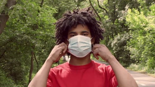 Man in Red Shirt Wearing Mask While Walking in Public Park During Summer