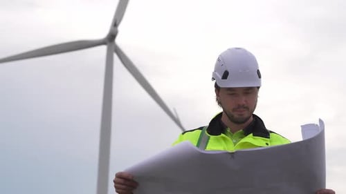 Worker reviews plans at wind farm site in the afternoon light