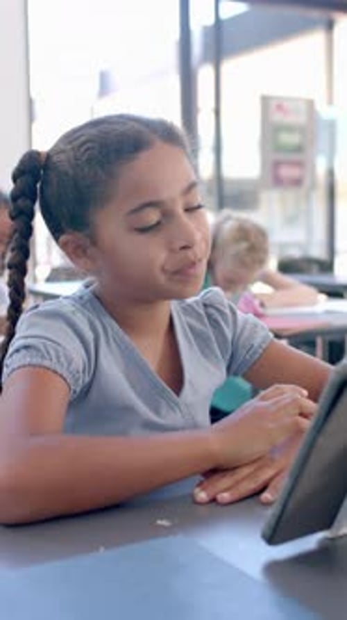 Vertical video: In school, young girl with a braid focusing on a tablet