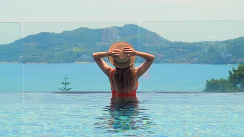 Back View of a Woman in a Hat Enjoying Travel Holiday at a Resort Pool
