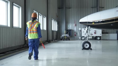 Mujer alguacil de vuelo caminando en el hangar de un avión para adultos