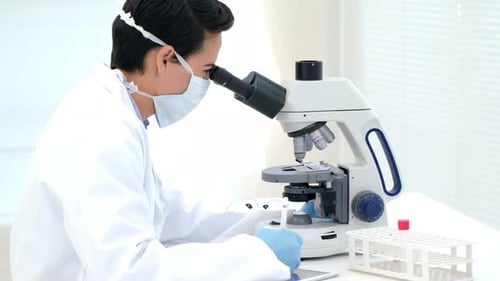 Scientist Using Microscope and Taking Notes in Lab