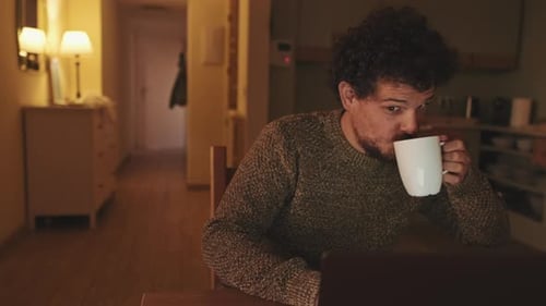 Man Using Laptop and Drinking Coffee at Home