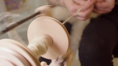 Woman operates modern treadle spinning wheel, spinning yarn from wool