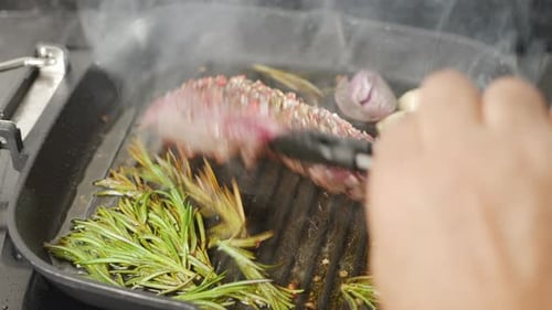 Chef flipping ribeye steak on the grill pan close-up.
