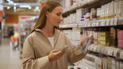 A Woman is Shopping in a Grocery Store She is Looking at the Shelves and She is Holding a Bottle of