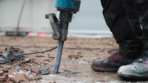 Man worker with jackhammer machine destroying asphalt or concrete road - close-up - reveal shot